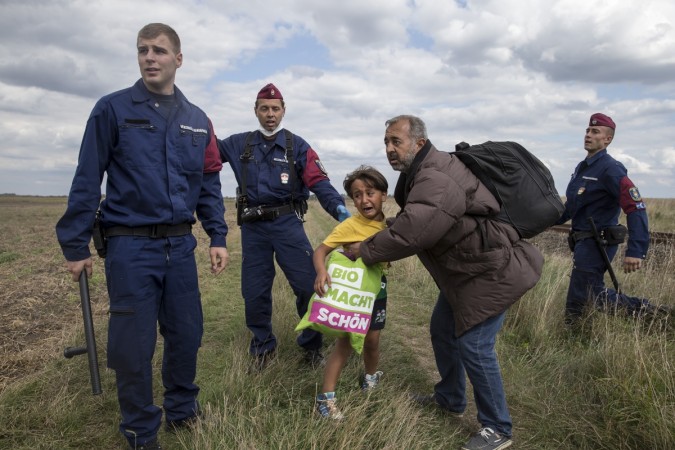 A migrant carrying a child falls after tripping on a TV camerawoman (R) while trying to escape from a collection point in Roszke village, Hungary, September 8, 2015.