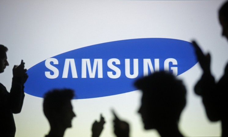 People pose with mobile devices in front of a screen projected with a Samsung logo