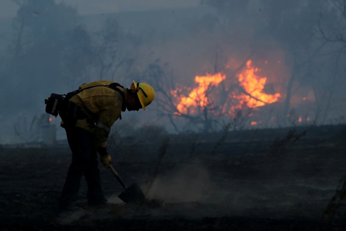 A firefighter works to put out hot spots on a fast moving wind driven wildfire in Orange. California wildfires