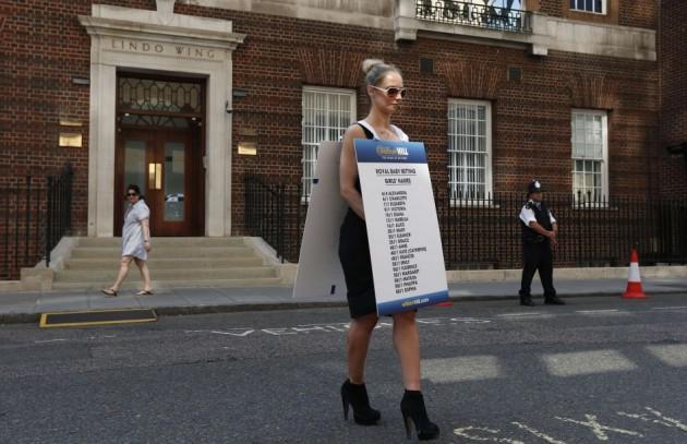 A woman wearing a betting shop odds board, printed with Royal Baby names, walks past the Lindo Wing of St Mary's Hospital, where Britain's Catherine, Duchess of Cambridge is due to give birth, in London Royal Fan