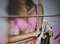A woman in hijab walks past a lingerie ad.