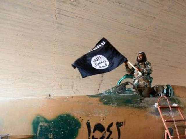 An Isis fighter waves the black flag of the Islamic State militant group standing inside the cockpit of a Syrian fighter plane.