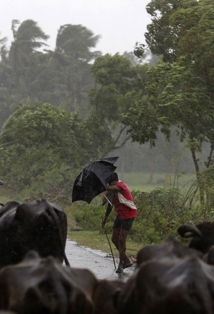 A boy tries to cover himself with an umbrella during heavy rain brought by Cyclone Phailin in Ichapuram town Cyclone Phailin