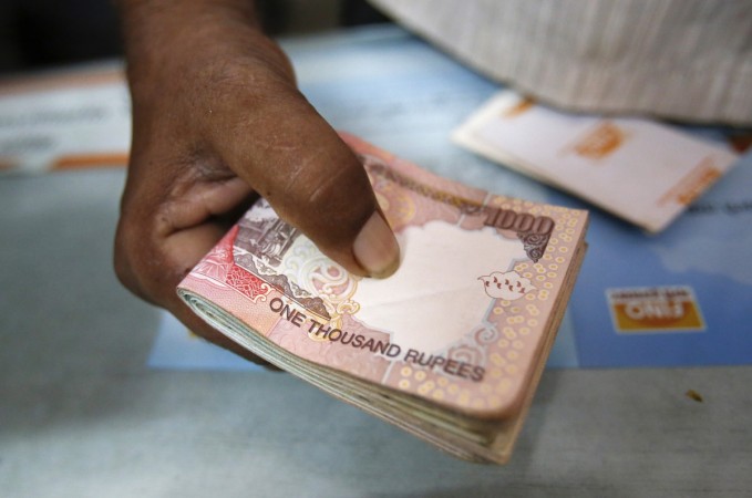 A customer hands a bundle of Indian Rupee currency notes to a teller at a financial institution in Mumbai