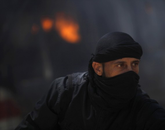A fighter from the Islamist Syrian rebel group Jabhat al-Nusra is seen in front of a burning vehicle.