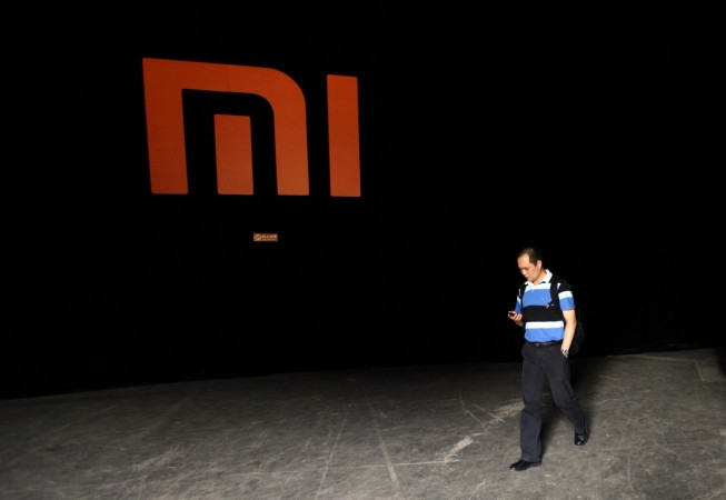 A man checks his mobile phone as he walks past a logo of Xiaomi during its Phone 2 launch ceremony in Beijing on August 16, 2012. Xiaomi