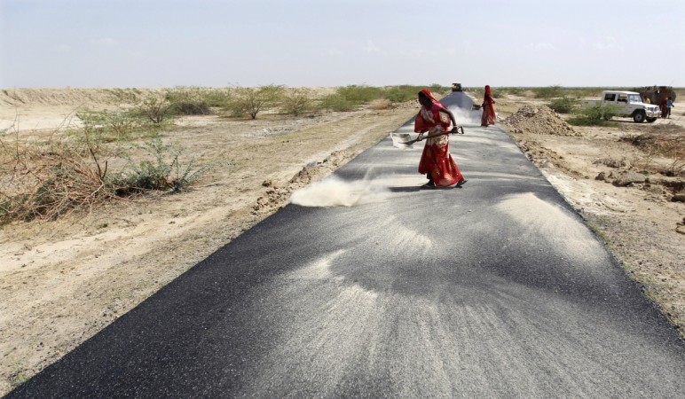 Women labourers throw dust on a road tarmac under construction at Bharadva village in the western Indian state of Gujarat. Road construction in India