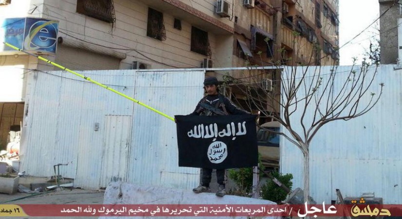 An Isis fighters poses with the black flag of the Sunni militant group inside Yarmouk camp.
