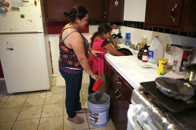 Marisela Corona, 26, (L) whose well has run dry, washes dishes with her daughter Andrea Andrade Corona, 8, from a water bucket in Porterville, California October 14, 2014.