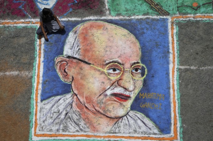 A man sits next to a painting of Mahatma Gandhi in Chennai. Mahatma Gandhi
