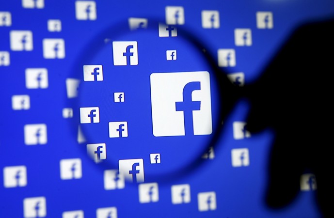 A man poses with a magnifier in front of a Facebook logo on display December 16, 2015. Facebook