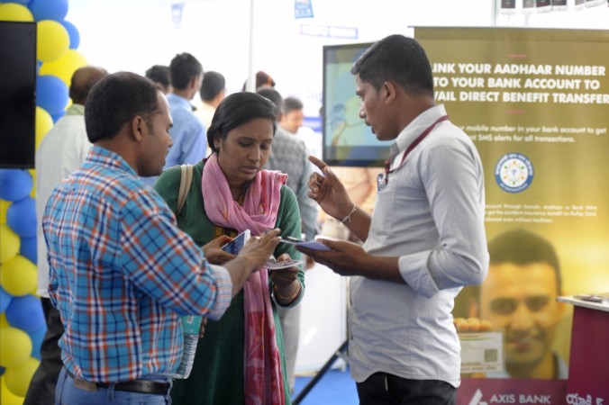 Indian visitors listen to a bank representative (R) regarding digital transactions with an Aadhaar or Unique Identification (UID) card during a Digi Dhan Mela, held to promote digital payment, in Hyderabad on January 18, 2017. aadhaar, aadhaar must for bank accounts, aadhaar opening bank accounts, aadhaar pan linkage