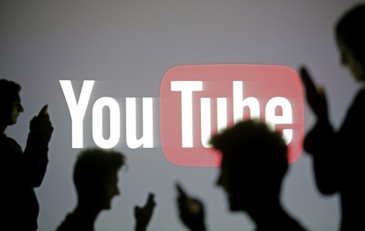 People are silhouetted as they pose with mobile devices in front of a screen projected with a YouTube logo. YouTube