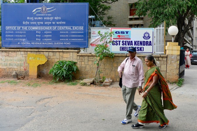 Pedestrians walk past a poster advertising the new goods and services tax (GST) regime at the Service Tax Office in Bangalore on June 29, 2017. gst, gst council, gst rate, gst tax, gst arun jaitley, gst modi govt, gst all you need to know