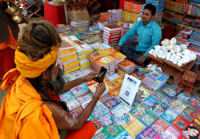 A Sadhu or a Hindu holy man pays the vendor through Paytm, a digital wallet company, after buying a book during the annual religious festival of Magh Mela in Allahabad Megh mela