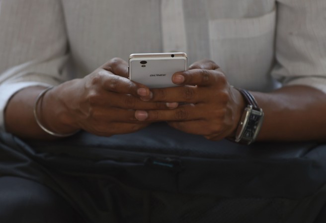 This photo taken on March 7, 2017 shows an Indian office worker checking his smartphone while waiting at a bus stop in Mumbai. smartphones India