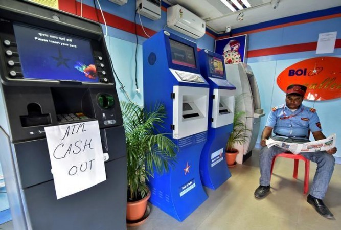 A security guard reads a newspaper inside an ATM counter as a notice is displayed on an ATM in Guwahati, India. atm cash shortage
