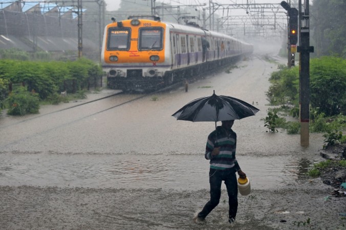 A man carrying an umbrella walks past a passenger train that moves through a water-logged track during heavy rains in Mumbai Mumbai rain
