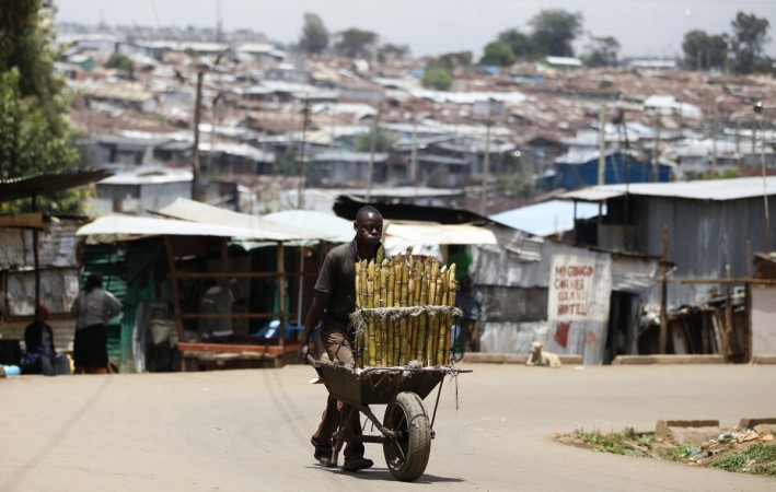 A trader pushes wheelbarrow loaded with sugar-cane for sale along a street in Kibera slum in Kenya sugar cane kenya