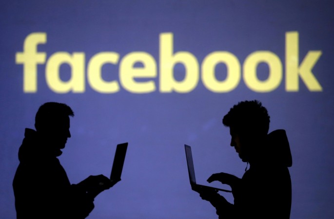 Silhouettes of laptop users are seen next to a screen projection of Facebook logo Facebook