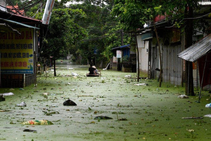 People row in a boat through floodwaters in Hanoi's suburban Chuong My district on August 2, 2018. - Heavy rains have flooded the area over the past 10 days. (Photo by Nhac NGUYEN / AFP) VIETNAM-WEATHER-DISASTER