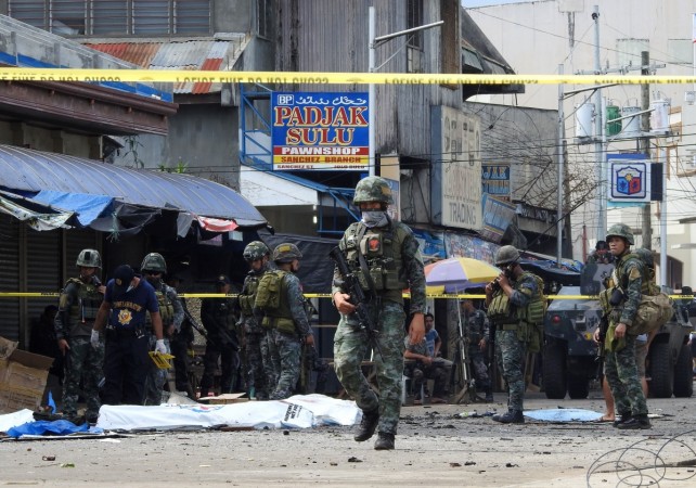 Policemen and soldiers keep watch as body bags (in white), containing the remains of blast victims, as seen in a cordoned area outside a church in Jolo, Sulu province on the southern island of Mindanao, on January 27, 2019. - At least 18 people were killed when two bombs hit a church on a southern Philippine island that is a stronghold of Islamist militants, the military said on January 27, days after voters backed the creation of a new Muslim autonomous region. Policemen and soldiers keep watch as body bags (in white), containing the remains of blast victims, as seen in a cordoned area outside a church in Jolo