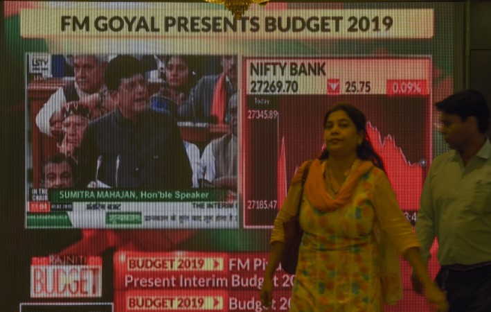 Office workers walk past a digital broadcast at the Bombay Stock Exchange showing Indian Finance Minister Piyush Goyal presenting the budget in parliament New Delhi, in Mumbai on February 1, 2019. INDIA-ECONOMY-BUDGET