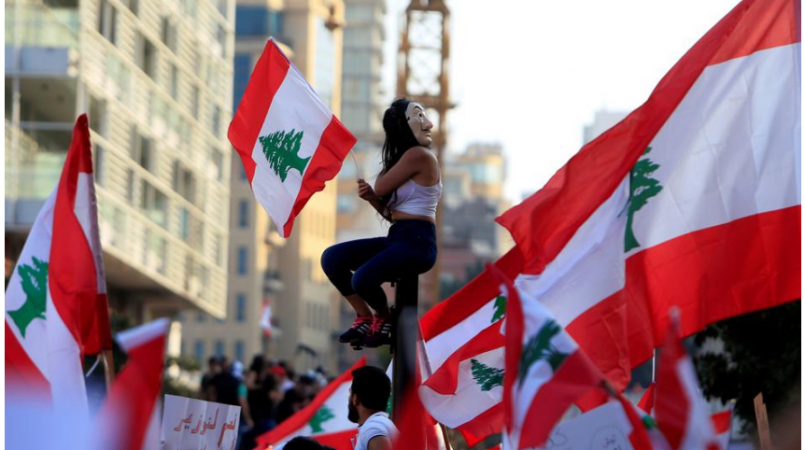 A demonstrator sits on a pole while carrying a national flag during an anti-government protest in downtown Beirut, Lebanon October 20, 2019. lebanon protest