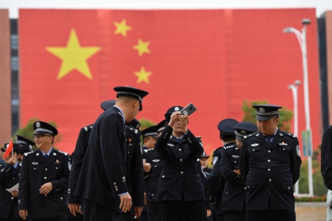 A police officer in front of a giant Chinese flag takes pictures with a mobile phone outside an exhibition. Facial recognition