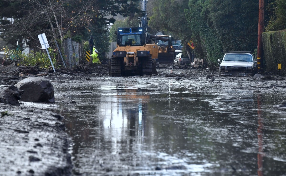 A car remains stuck in the mud as a cleanup crew work to clear mud beside a closed off section of US Hwy 101 California mudslides