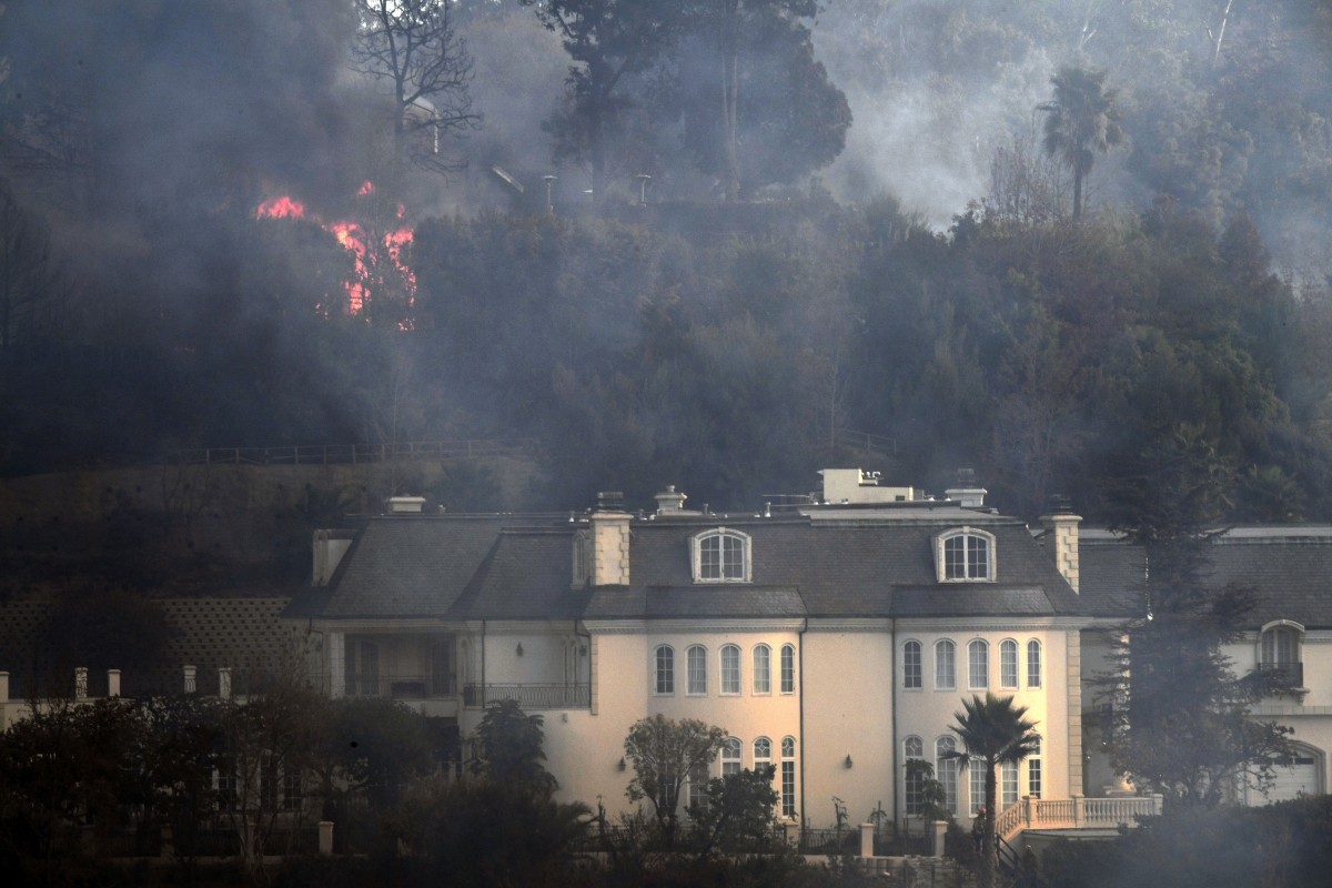Flames are seen behind a Bel Air mansion threatened by the Skirball Fire in west Los Angeles, California on December 6, 2017 Skirball Fire