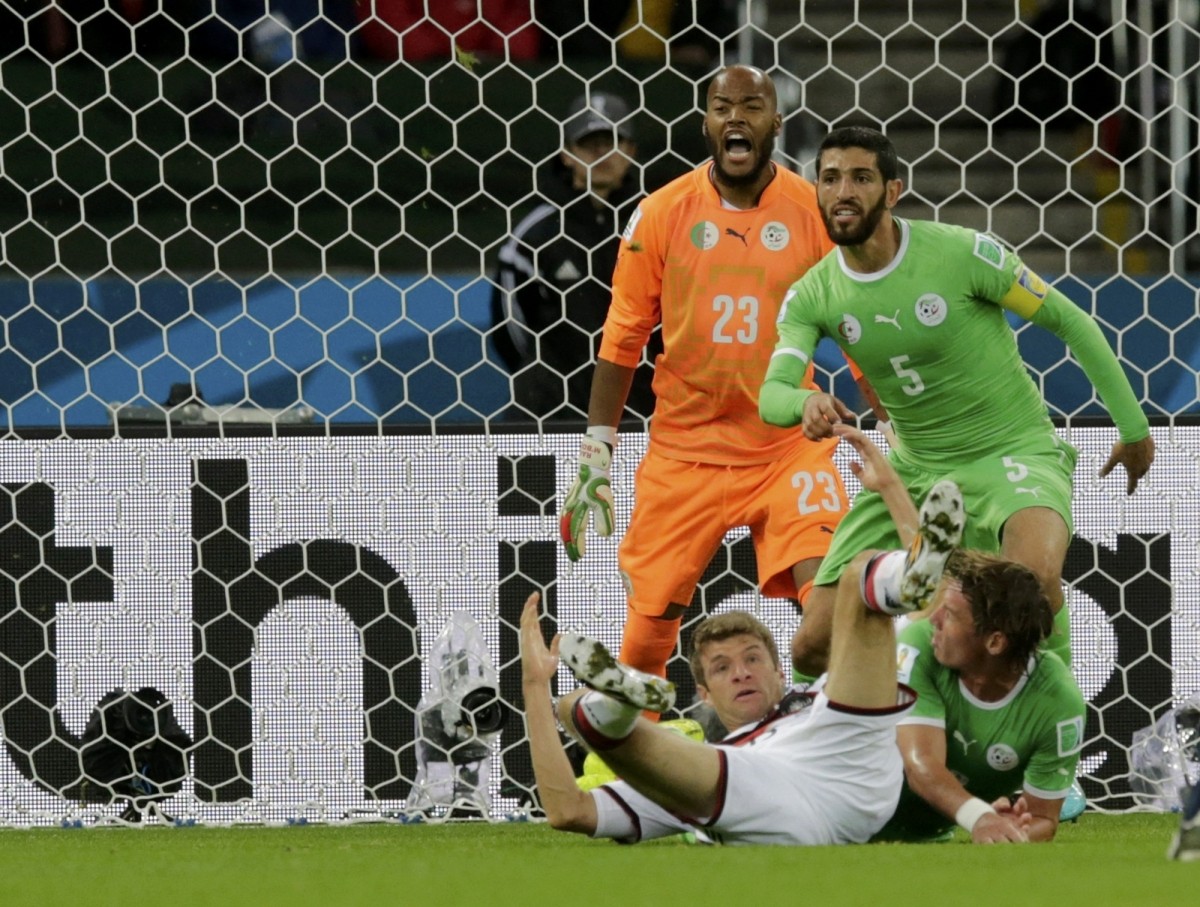 Germany's Thomas Mueller falls to the ground as Algeria's Rafik Halliche and Rais Mbolhi keep their eye on the ball during their 2014 World Cup round of 16 game at the Beira Rio stadium in Porto Alegre Germany vs Algeria