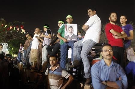 A supporter of Egypt's deposed President Mohamed Mursi holds a poster of him (C) while waiting with others as prayers are performed, during their sit-in outside the Rabaa Adawiya mosque, east of Cairo July 11, 2013.