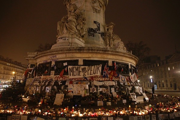 A photo taken on December 13, 2015 shows a sign (C) reading 'Not even afraid' and flowers, flags and candles placed at the foot of the the central monument on the Place de la Republique in Paris, in memory of the victims of the November 13 attacks which left 130 people dead. / AFP / MATTHIEU ALEXANDRE FRANCE-ATTACKS-MEMORIAL