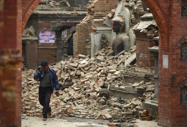 A man cries as he walks on the street while passing through a damaged statue of Lord Buddha a day after an earthquake in Bhaktapur, Nepal April 26, 2015.