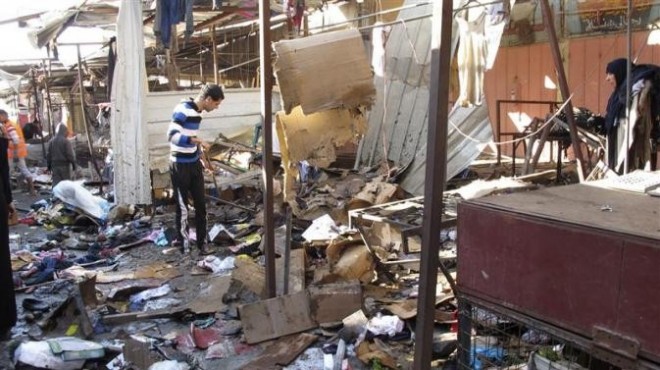 People stand among debris at the site of a bomb attack at a marketplace in Baghdad's Doura District December 25, 2013.