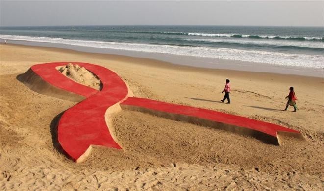 People walk near a red ribbon sand sculpture created by Indian sand artist Sudarshan Patnaik in Odisha. World AIDS Day