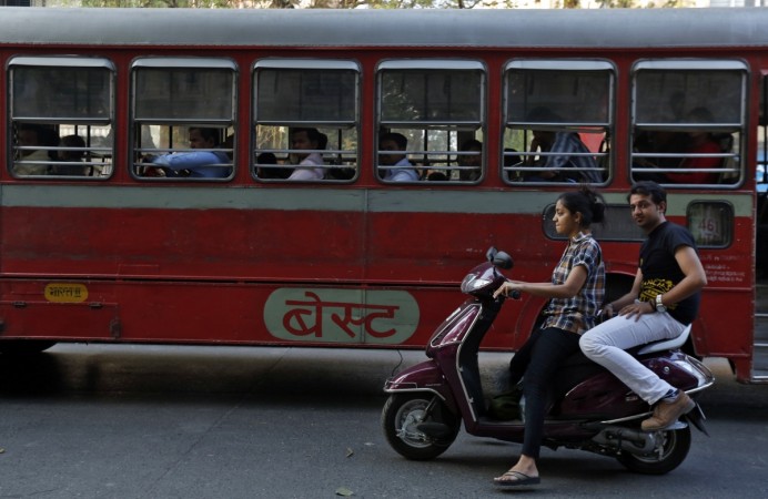 Ashok Leyland manufactures buses and trucks. A woman rides a scooter past a passenger bus on a street in Mumbai February 5, 2014 (representational image). ashok leyland sales commercial vehicles september buses share price fall demand weak row in a domestic tata motors