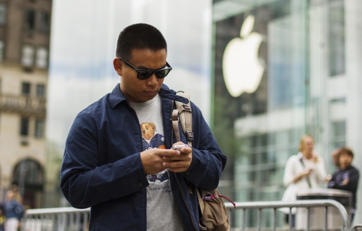 A man types on his Apple iPhone as he walks past an Apple logo hanging in a glass enclosure above the 5th Ave Apple Store in New York. iPhone man typing