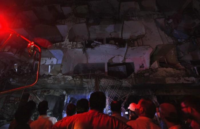 Residents stand in front of a damaged building after a bomb blast in a residential area in Karachi
