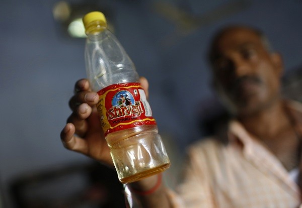A policeman in civilian clothes shows a bottle containing oil which they recovered from the school where contaminated meals were served to children on 16 July, at a police station in Masrakh at Chapra district of the eastern Indian state of Bihar.