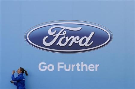 A woman has a drink as she walks past a logo of carmaker Ford at the entrance to a media event for the launch of a concept car in Sydney August 13, 2013.