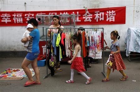 A family walk past a vendor selling women's clothes along a market street at a residential area for migrant workers in Beijing