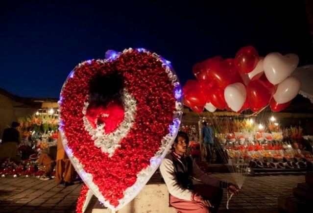 A man sits on a roadside next to a paper-flower decoration as he holds heart-shaped balloons, waiting for costumers on the ahead of Valentine's Day in Islamabad February 13, 2014. (Reuters) Valentine's Day