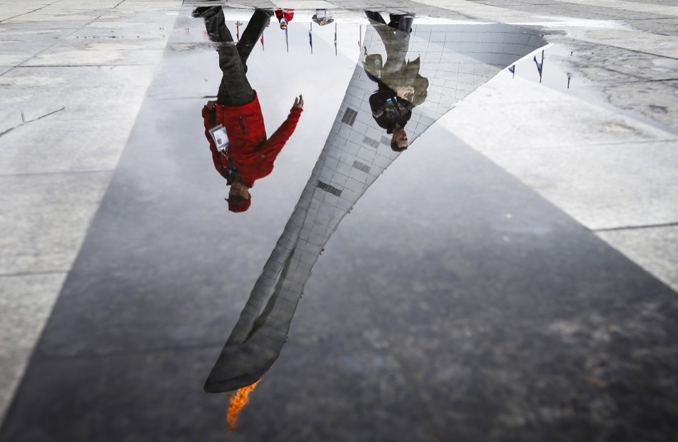 Fans walking past the Olympic Cauldron and flame are reflected in a puddle in the Olympic Park during the 2014 Winter Olympic Games in Sochi, February  Olympic Flame