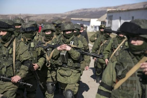 Military personnel, believed to be Russian servicemen, walk outside the territory of a Ukrainian military unit in the village of Perevalnoye outside Simferopol.