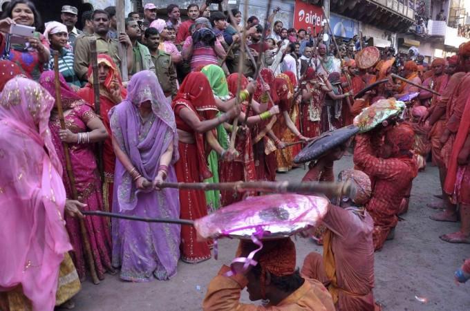 A group of women beat men holding a shield over their heads during Lathmar Holi
