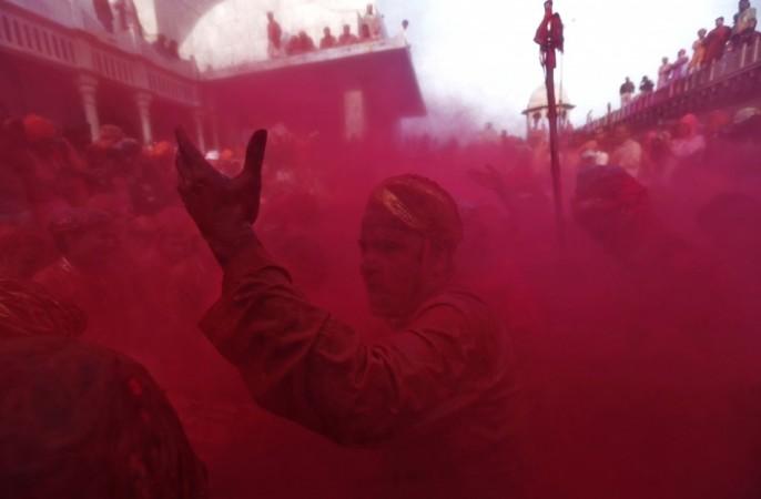 A man covered in coloured powder sings a hymn at a temple during Lathmar Holi