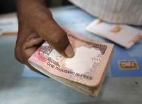A customer hands a bundle of Indian Rupee currency notes to a teller at a financial institution in Mumbai