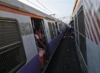 Passengers ride at the open doorways of commuter trains in Mumbai